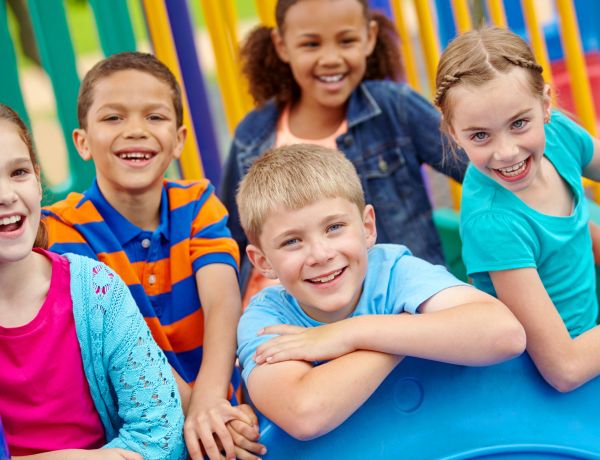 Fünf Grundschulkinder lachen gemeinsam auf einem farbenfrohen Klettergerüst auf dem Schulhof