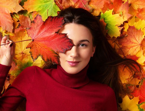 Frau mit rotem Pullover in bunten Herbstblättern