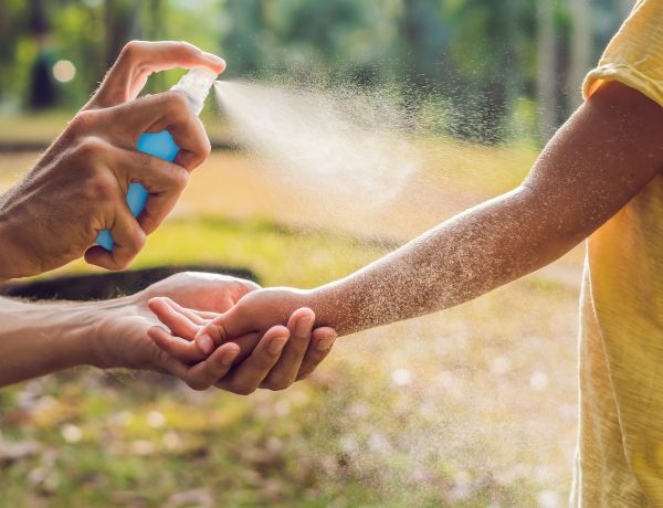 Hand wird mit Insektenspray eingesprüht zum Schutz vor Mücken und Zecken im Sommer