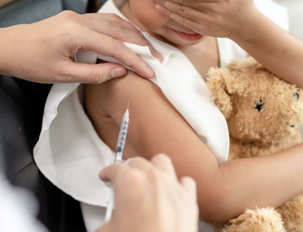 Kind erhält Impfung am Oberarm, hält Teddy im Arm – Impfprävention für Kinder und Erwachsene