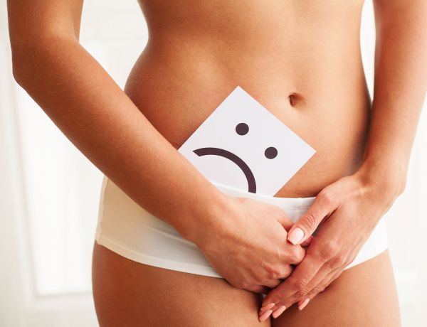 Frau hält Zettel mit traurigem Smiley vor dem Bauch – Symbolbild für Harnwegsinfektion im Sommer