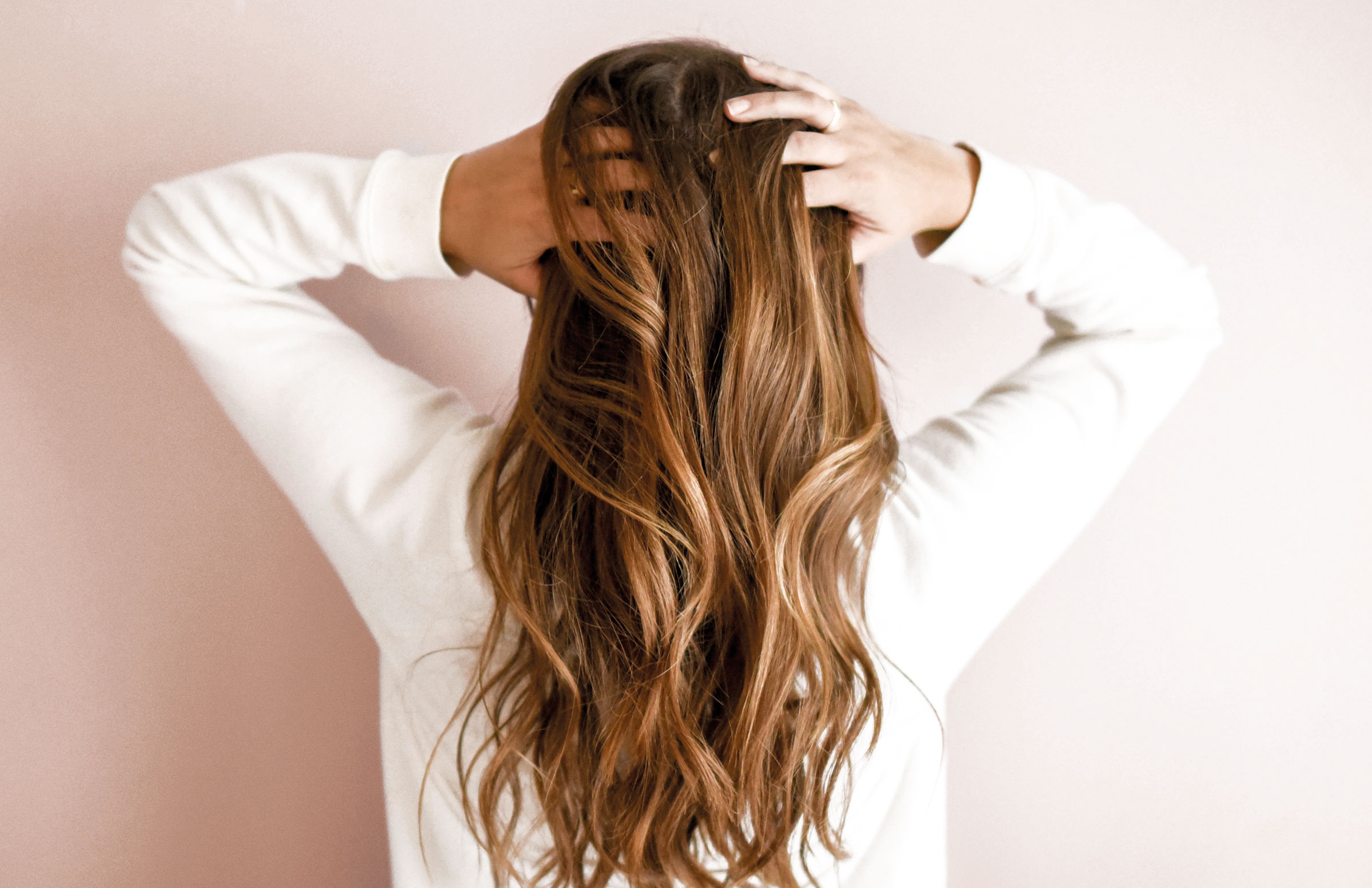 Frau mit langen braunen Haaren steht mit dem Rücken zur Kamera und hält sie zusammen.