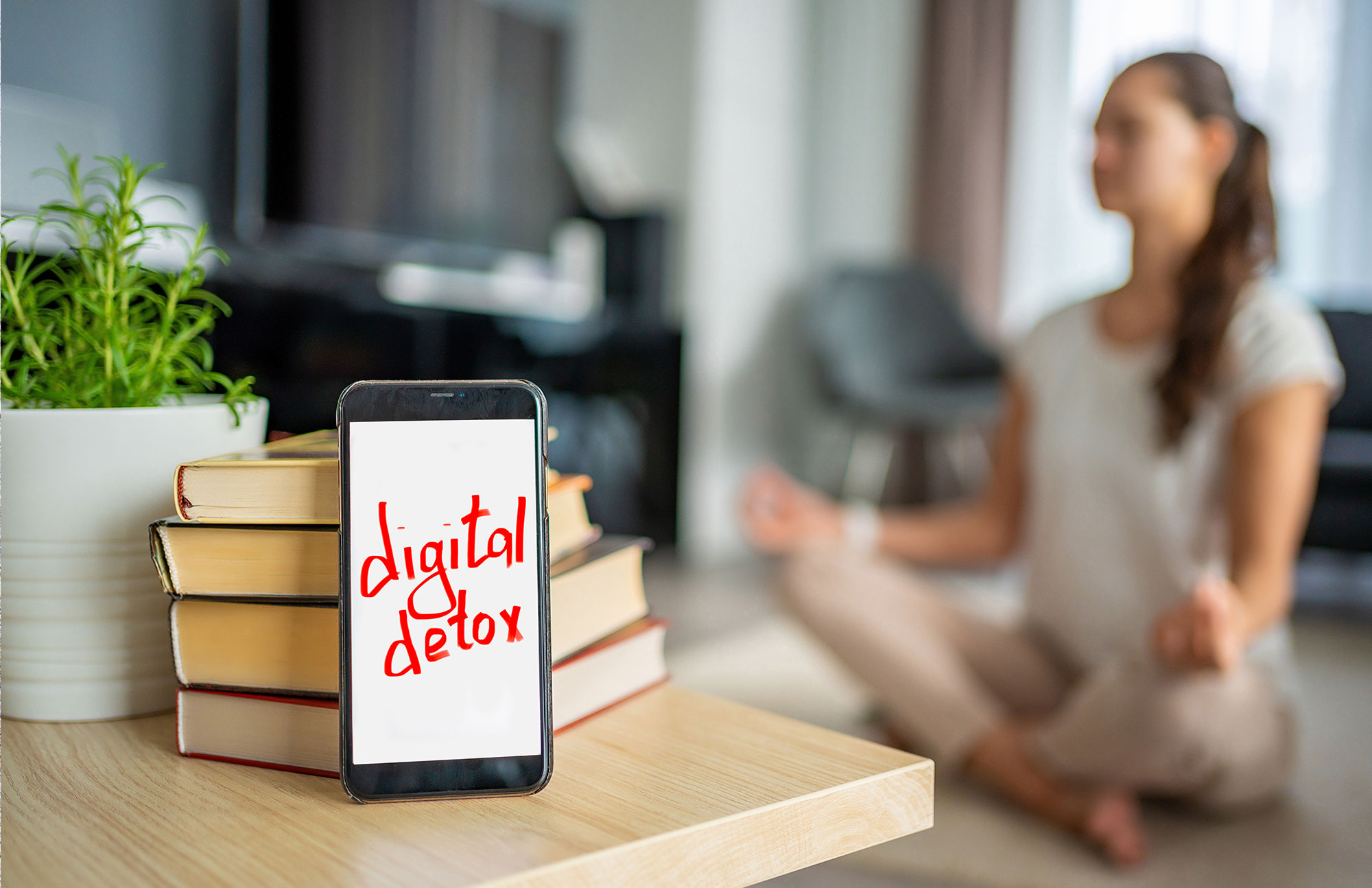 Frau macht Yoga-Übung, davor steht ein Schild mit dem Wort „Digital Detox“.