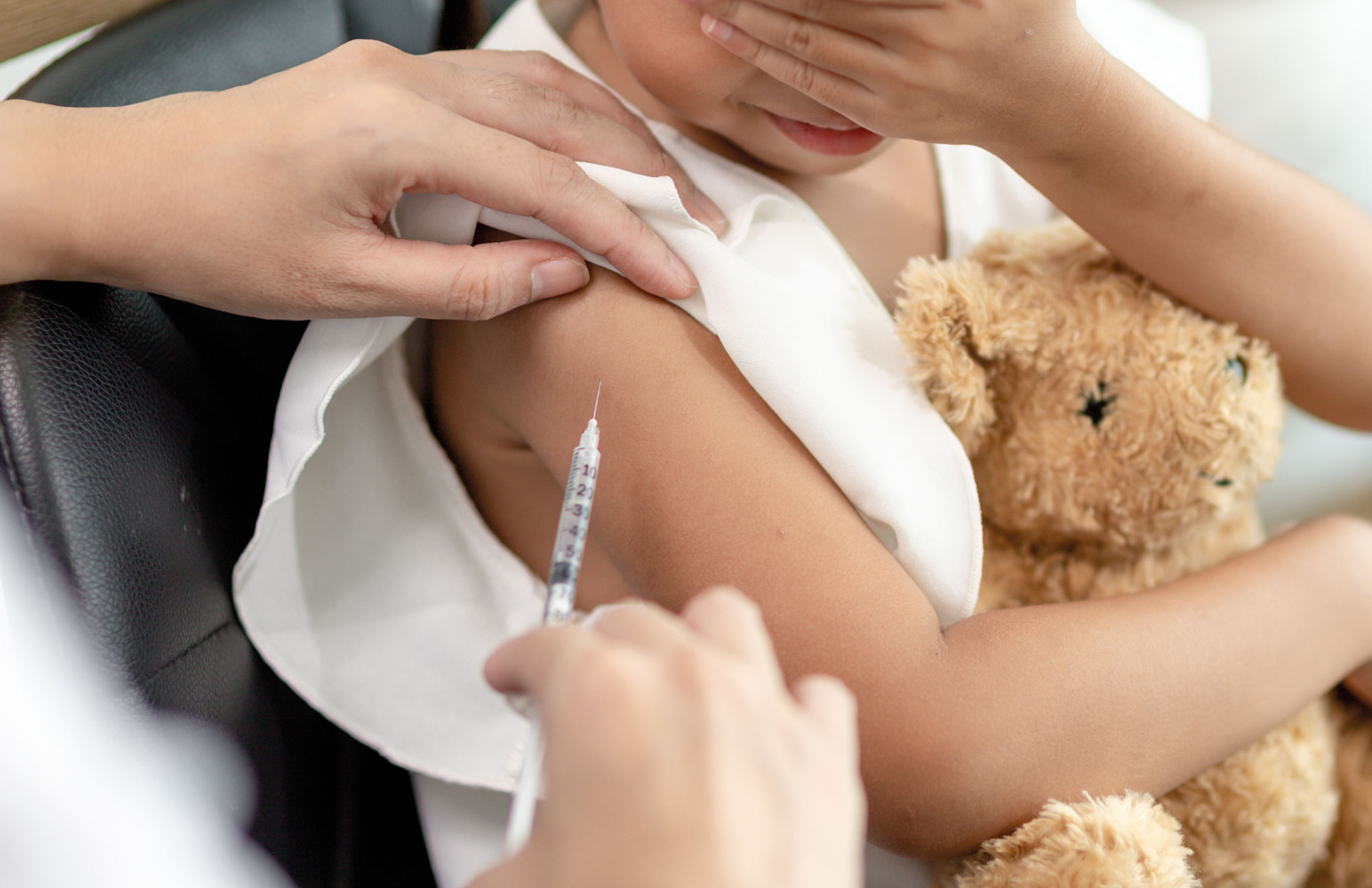 Kind erhält Impfung am Oberarm, hält Teddy im Arm – Impfprävention für Kinder und Erwachsene