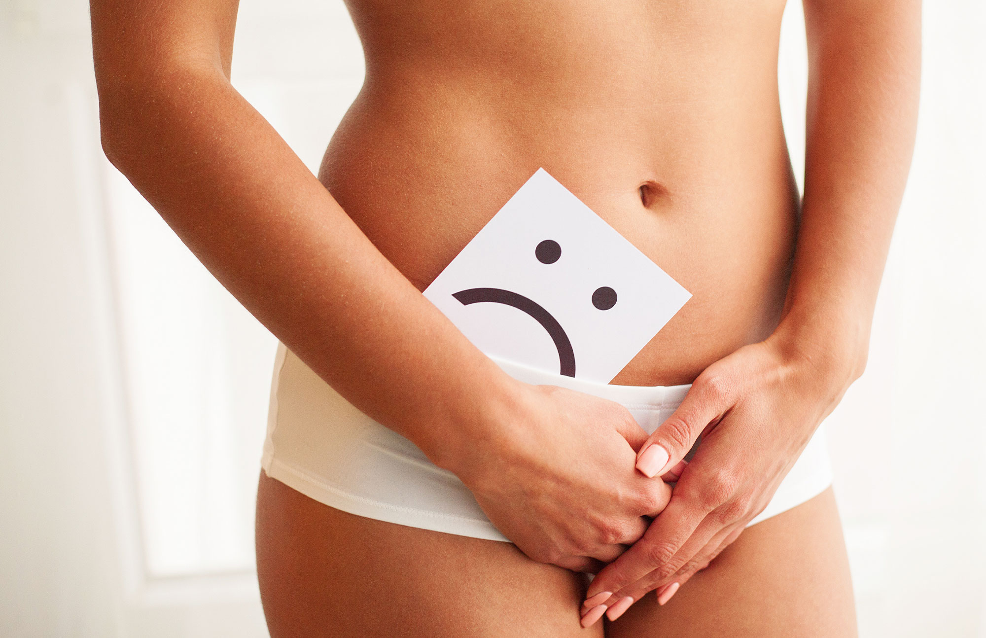 Frau hält Zettel mit traurigem Smiley vor dem Bauch – Symbolbild für Harnwegsinfektion im Sommer