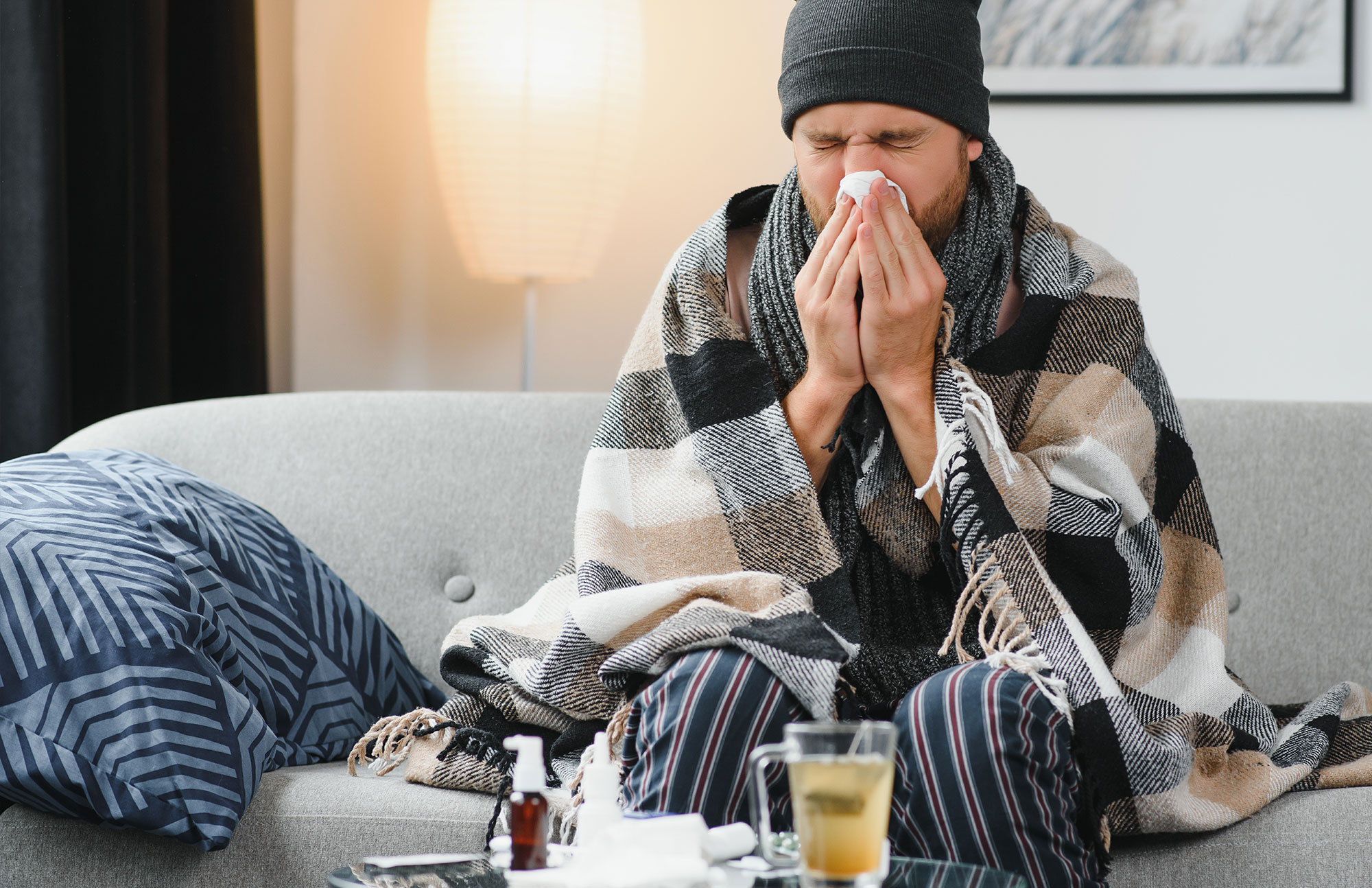 Mann krank auf Sofa mit Decke und Taschentuch