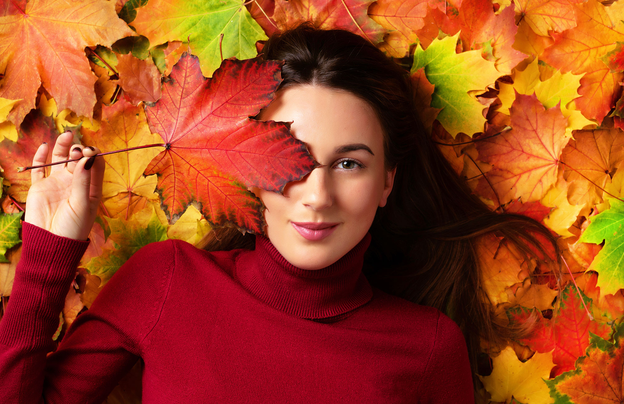 Frau mit rotem Pullover in bunten Herbstblättern