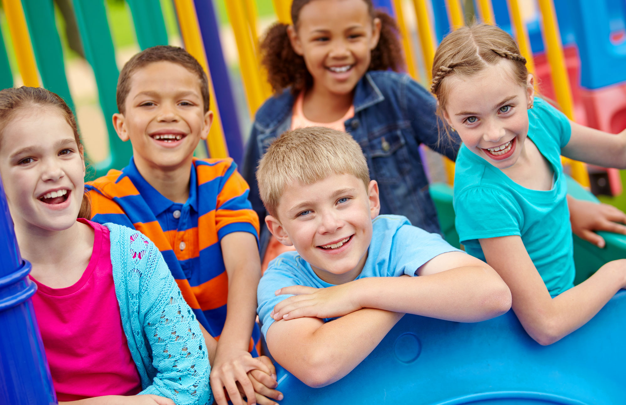 Fünf Grundschulkinder lachen gemeinsam auf einem farbenfrohen Klettergerüst auf dem Schulhof