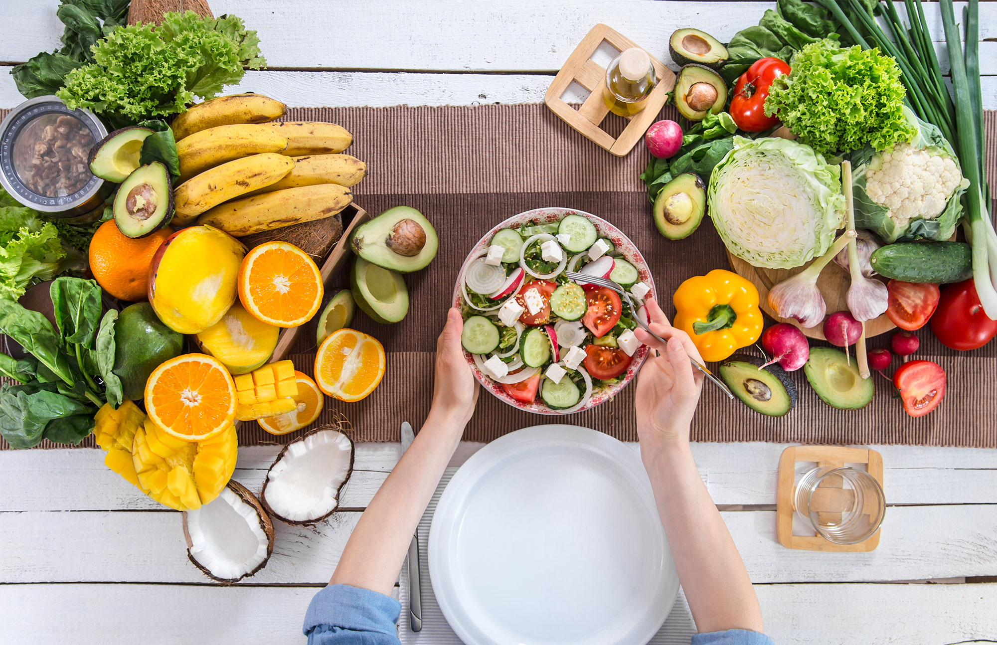 Draufsicht auf gedeckten Tisch mit Schüssel Salat, umgeben von Obst, Avocados und verschiedenem Gemüse.
